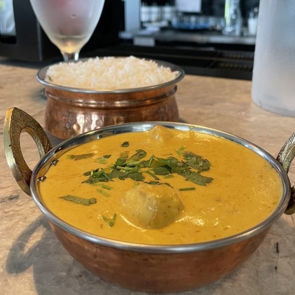 Jhapali Kitchen & Bar's Nepalese curry in a copper bowl with rice, garnished with cilantro.
