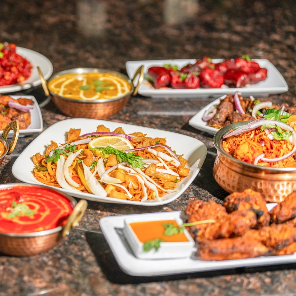 A variety of colorful Nepalese dishes, including noodles, curries, and rice, arranged on a dark table.
