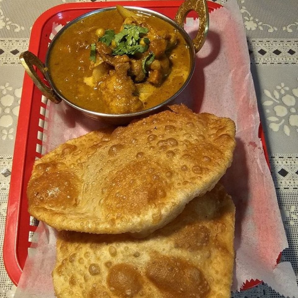 Nepalese chicken curry in a brass bowl with two pieces of fried bread (puri) on a red tray.