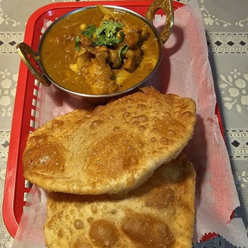 Nepalese chicken curry in a brass bowl with two pieces of fried bread (puri) on a red tray.