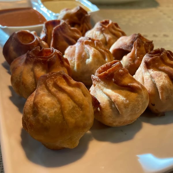 A plate of golden-brown fried Nepalese momo dumplings with two dipping sauces in the background.