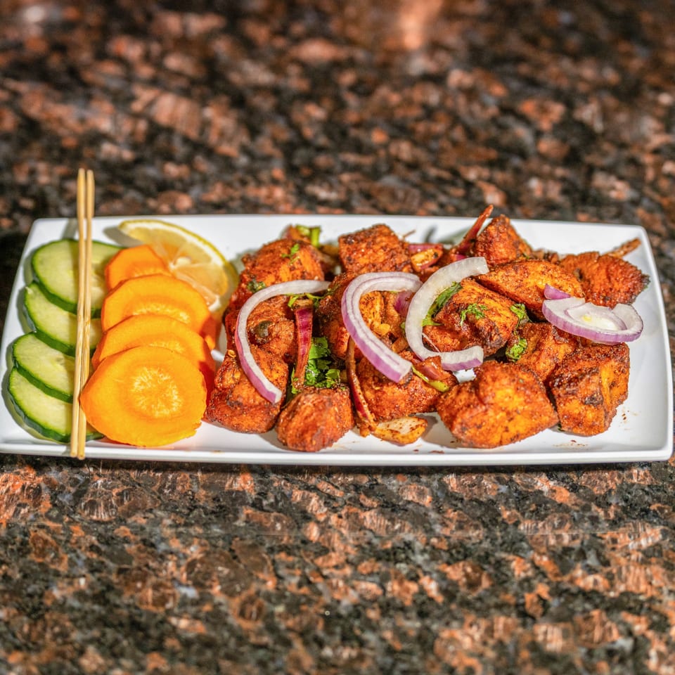 Jhapali Kitchen & Bar's Nepalese chicken choila, garnished with red onions, cilantro, and lemon.