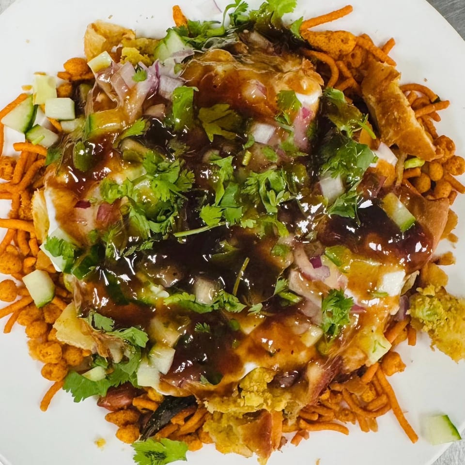 Nepalese chatamari dish topped with sauces, chopped onions, cucumbers, and cilantro on a white plate.