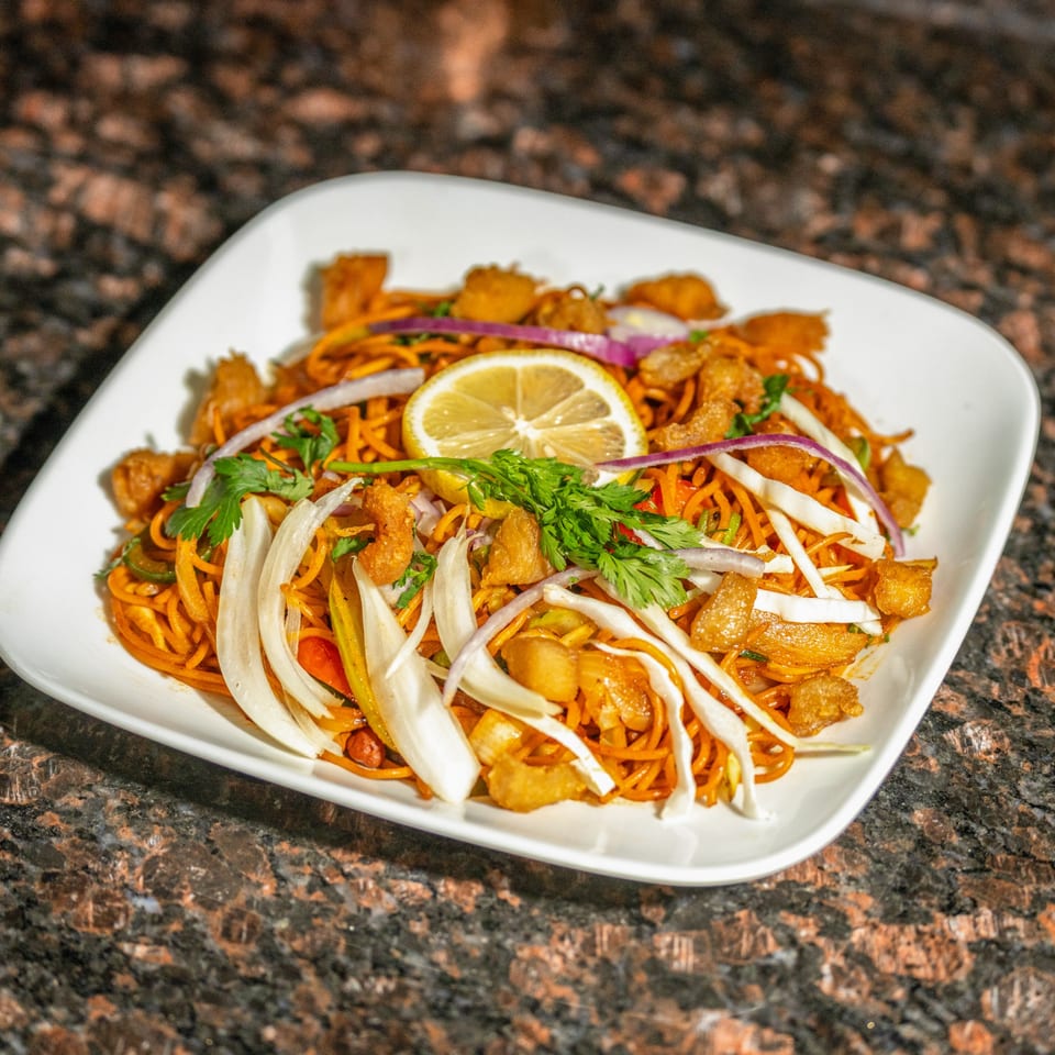 Nepalese chowmein with chicken, vegetables, and a lemon slice on a white plate.