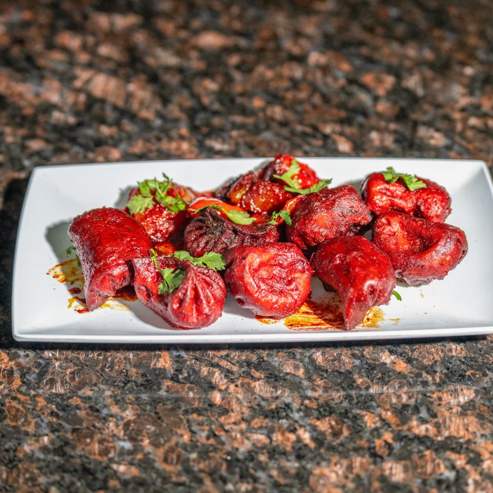 Red Nepalese momo dumplings with cilantro and chili oil on a white plate.