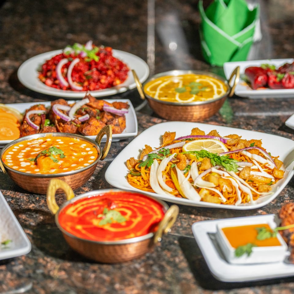A table laden with various colorful Nepalese dishes, including curries, noodles, and meat preparations.