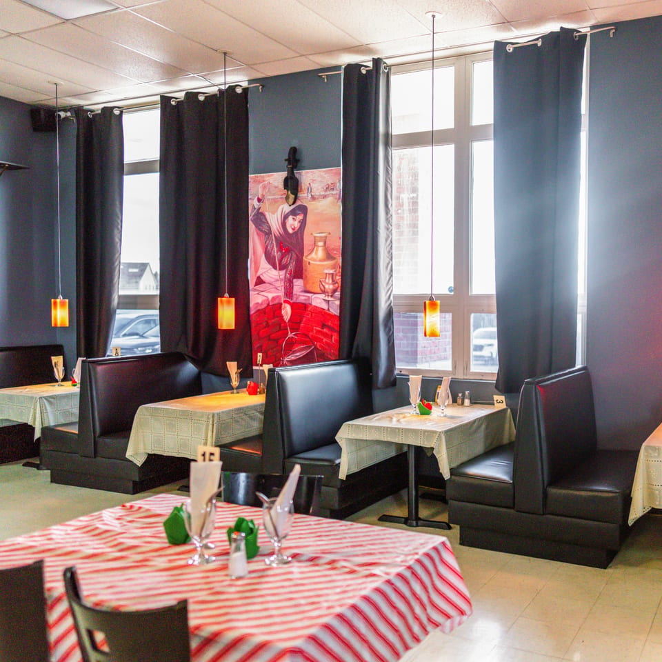 Interior of Jhapali Kitchen & Bar with black booths, tables with checkered cloths, and window views.