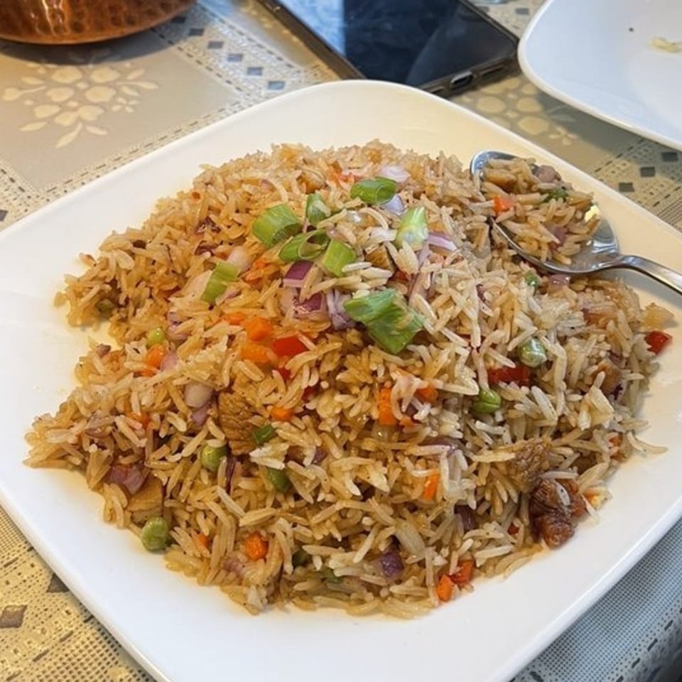 A white plate filled with Nepalese fried rice, garnished with chopped green onions and vegetables.