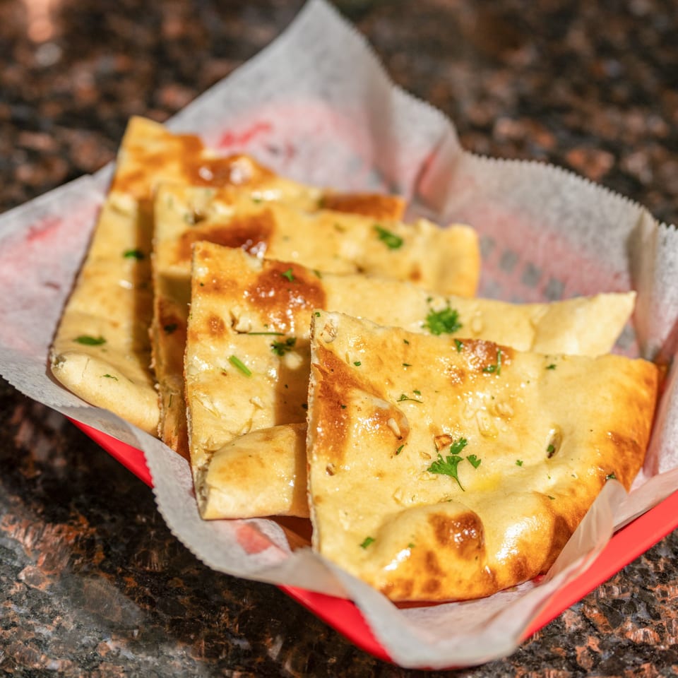 Golden brown garlic naan bread, garnished with parsley, served in a red basket lined with paper.