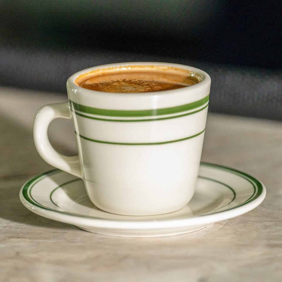 A white cup with green stripes and a matching saucer holds a dark beverage with foam.