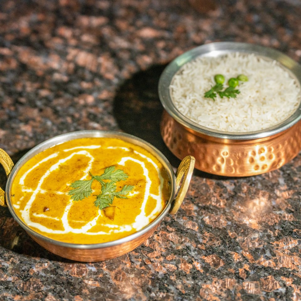 Two copper bowls of Nepalese food, one with yellow curry and the other with white rice.