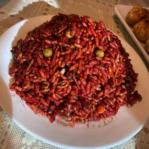 A close-up of a large serving of Jhapali Kitchen & Bar's red, spicy puffed rice with green peas.