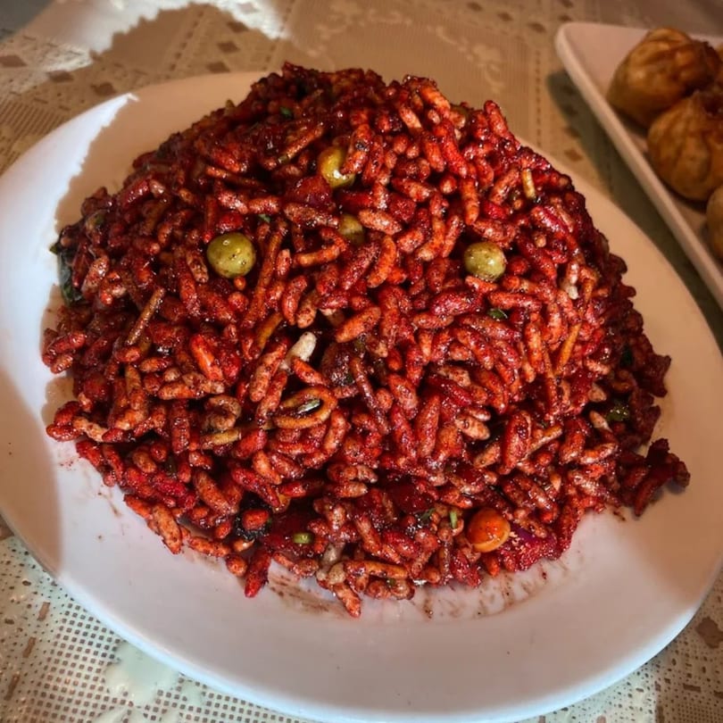 A close-up of a large serving of Jhapali Kitchen & Bar's red, spicy puffed rice with green peas.