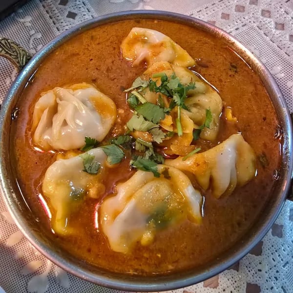 A close-up of Jhapali Kitchen & Bar's Nepalese momo dumplings in a rich, orange curry sauce.