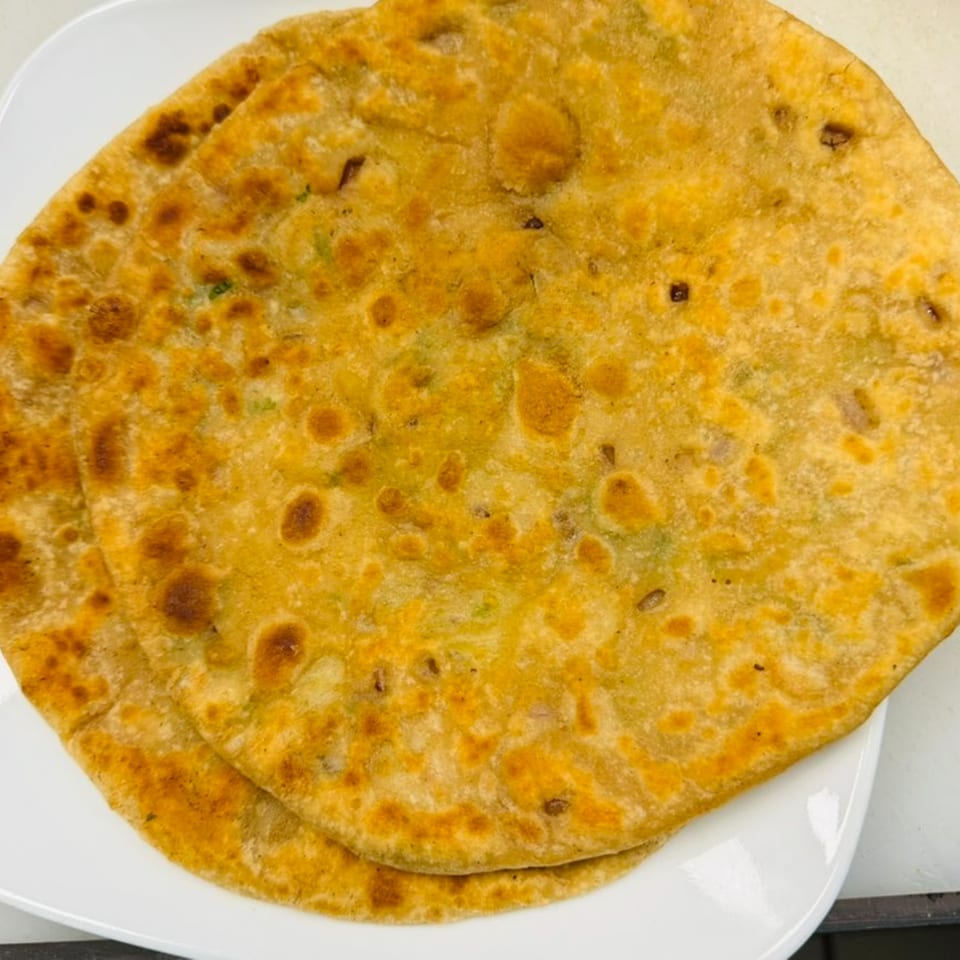 Two golden-brown Nepalese flatbreads, possibly paratha, with visible spices, on a white plate.
