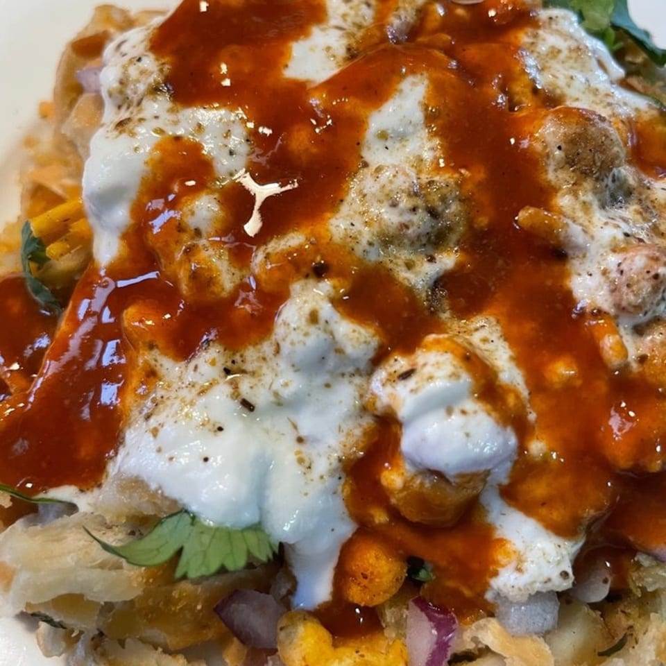 Close-up of a Nepalese dish with white yogurt, red sauce, and spices over a base of fried dough.